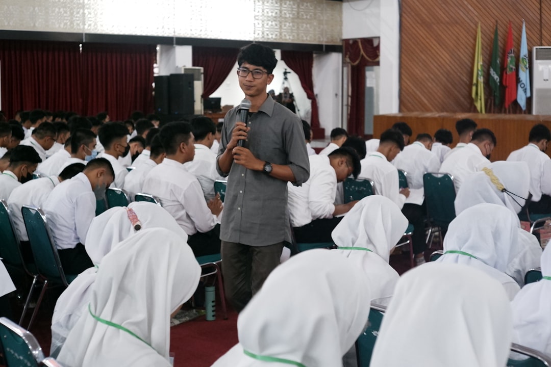 a-person-speaking-into-a-microphone-in-front-of-a-group-of-people-axwia92agr0